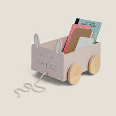 Children's toy cart with rabbit design holding books on a light beige background