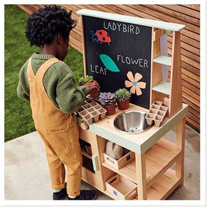 Young boy playing with outdoor wooden mud kitchen