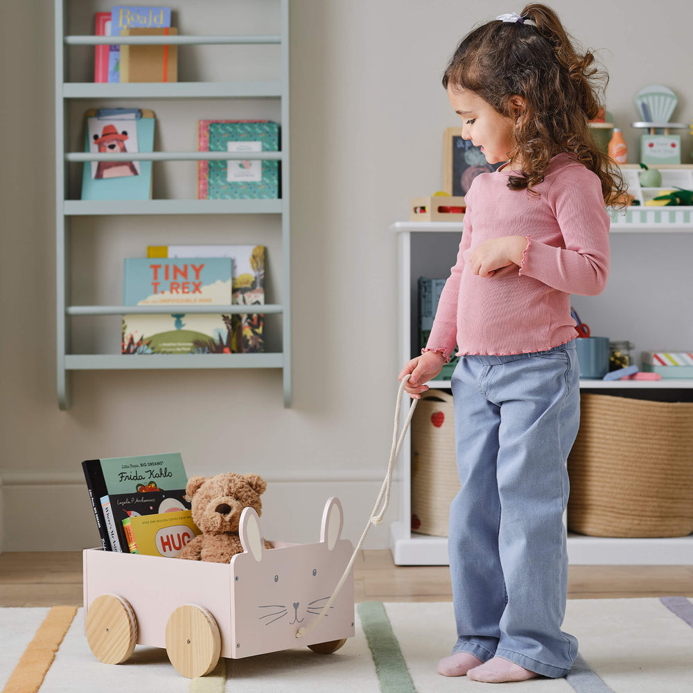 Children's toy cart with rabbit design holding books on a light beige background