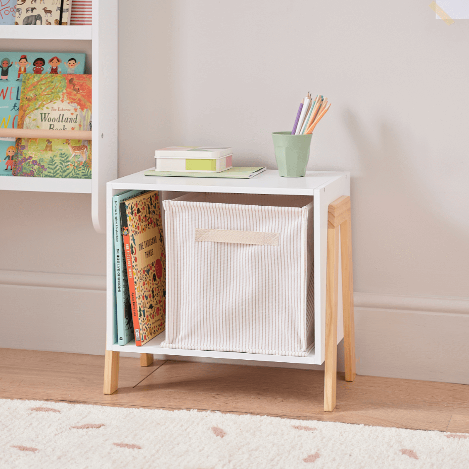Small white storage unit with a woven basket on a wooden floor, with books and a cup on top.