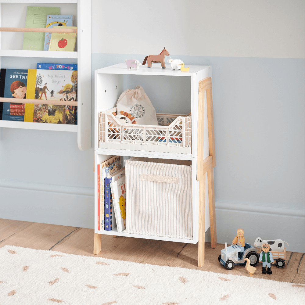 Small white storage unit with a woven basket on a wooden floor, with books and a cup on top.