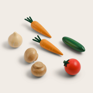A set of wooden toy vegetables including two orange carrots with green tops, a green cucumber, a red tomato with a green stem, a beige onion, and two light brown mushrooms, arranged on a light cream background.