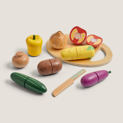 A set of wooden toy vegetables and a wooden knife on a light beige background. The set includes a yellow pepper, brown onion, red tomato halves, yellow carrot, green cucumber, purple eggplant, and a brown potato, along with a wooden cutting board and knife.