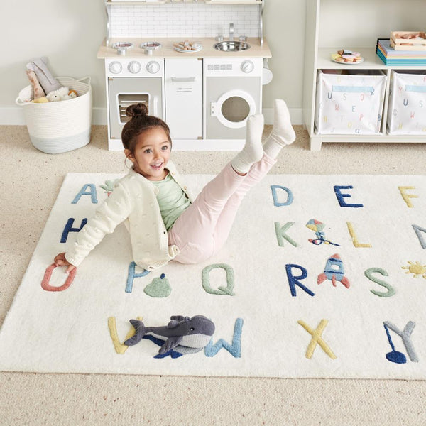 Child playing on a rug with letters and toys in a playroom setting