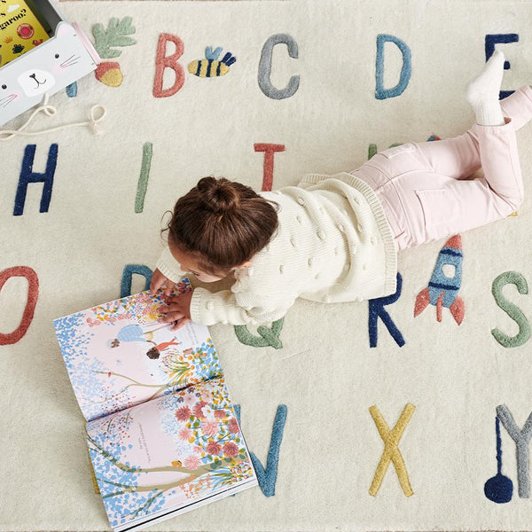 Child lying on a colorful alphabet rug reading a book