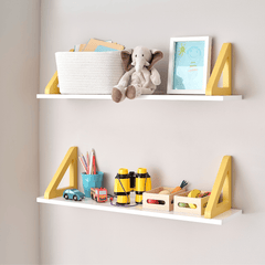 Two white wall shelves with yellow triangular brackets, styled with toys, a basket, a stuffed elephant, and a framed picture against a light gray wall.